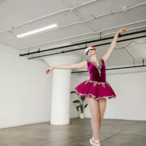 A ballerina in a vibrant outfit dances gracefully wearing a VR headset in a studio setting.